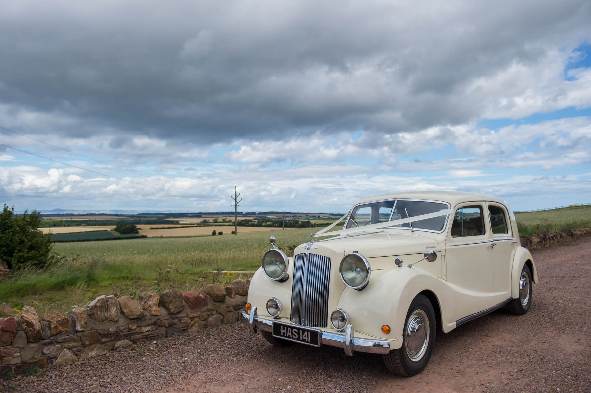 A white vintage car with a ribbon tied on to the front from Lothian Classic Wedding Cars